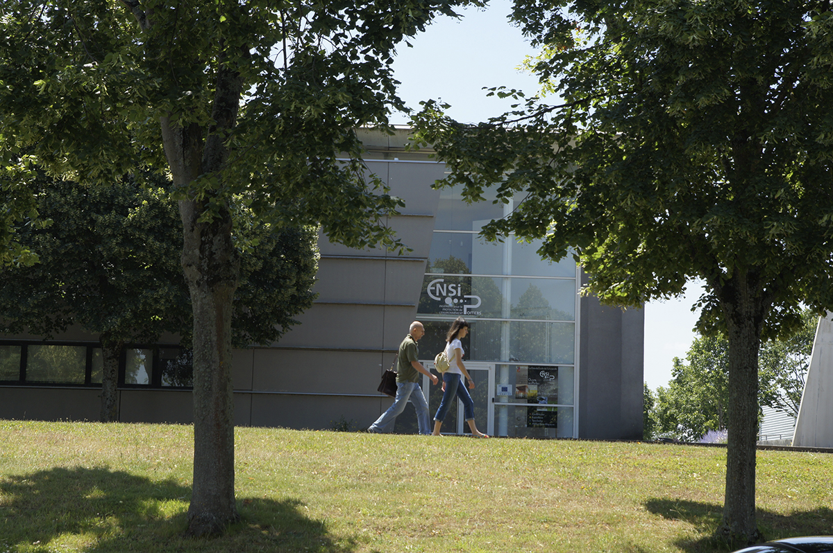Étudiants devant un bâtiment universitaire sur un campus arboré.