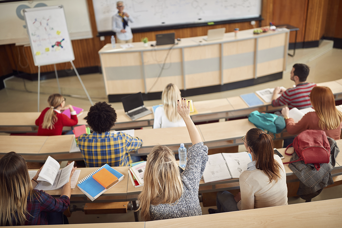 Étudiants dans un amphithéâtre, une main levée.